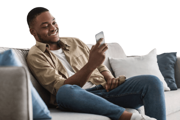 Man smiling while looking at his phone, sitting on a couch.
